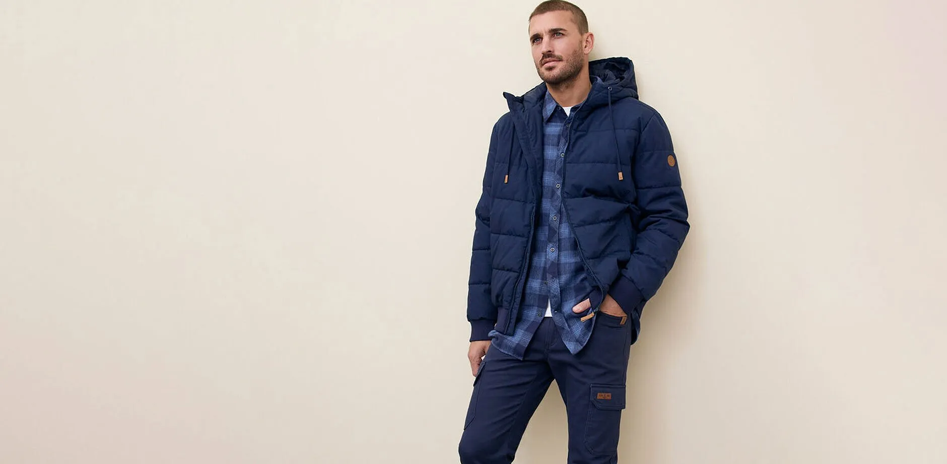 Marineblauwe gewatteerde jas, jeans en blauw geruit overhemd.