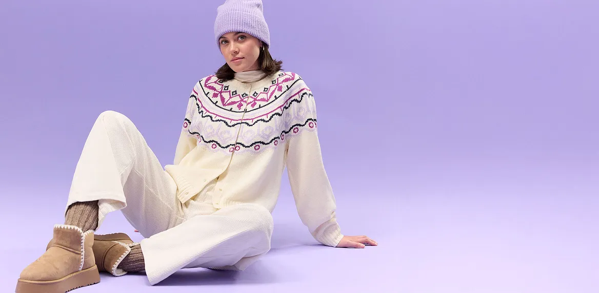 Crèmekleurige trui met Noors patroon, witte broek en lila gebreide muts.