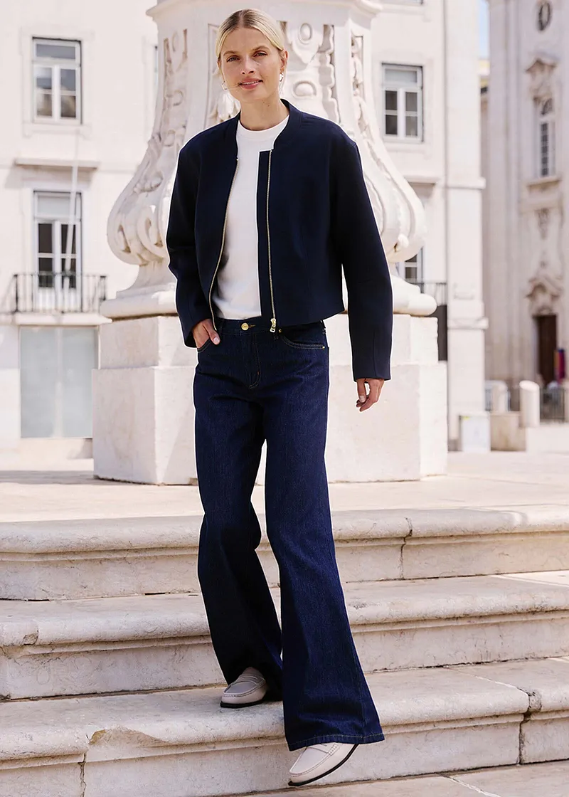 Elegante look met een donkere jas, wit shirt en wijde jeans.