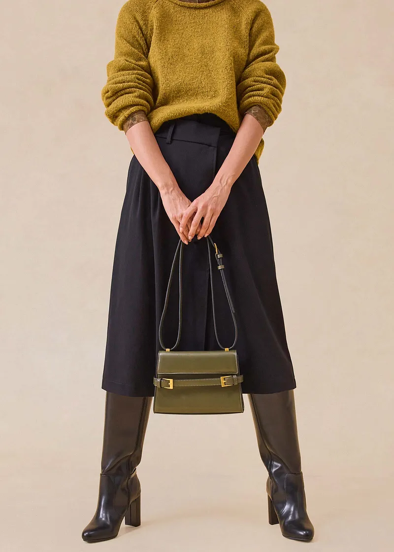Mosterdgele trui, zwarte midi rok, bruine laarzen en elegante handtas.