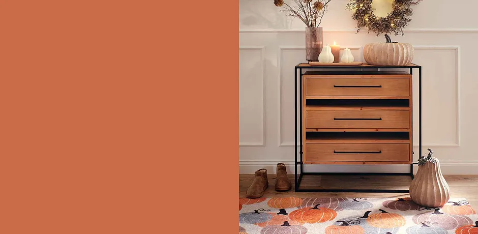 Houten ladekast met zwarte grepen, omgeven met herfstdecoraties en warme, aardse tinten.