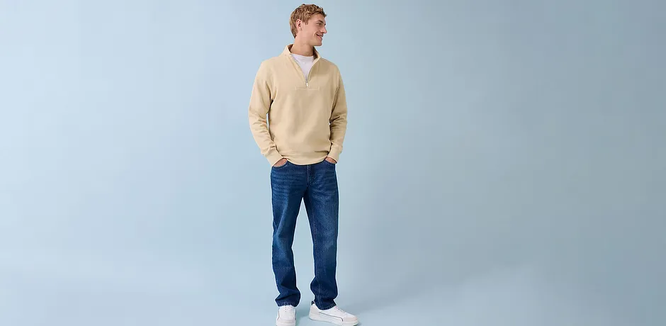 Informele stijl met een crèmekleurige trui, blauwe spijkerbroek en witte sneakers.