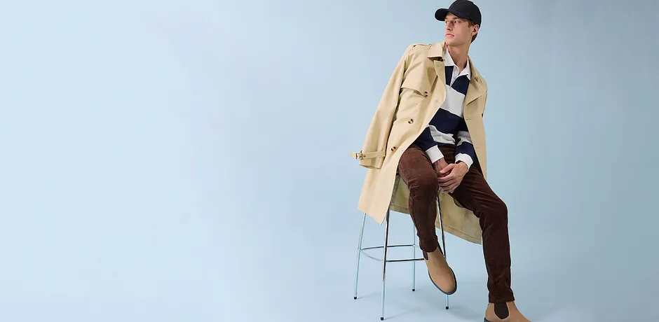 Stijlvolle trenchcoat, bruine broek en zwarte pet - een moderne look voor iedere dag.