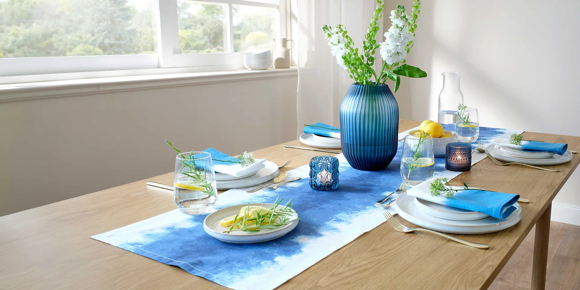Een blauwe tafelloper siert de eettafel, contrasterend met witte borden en kleurrijke accessoires.