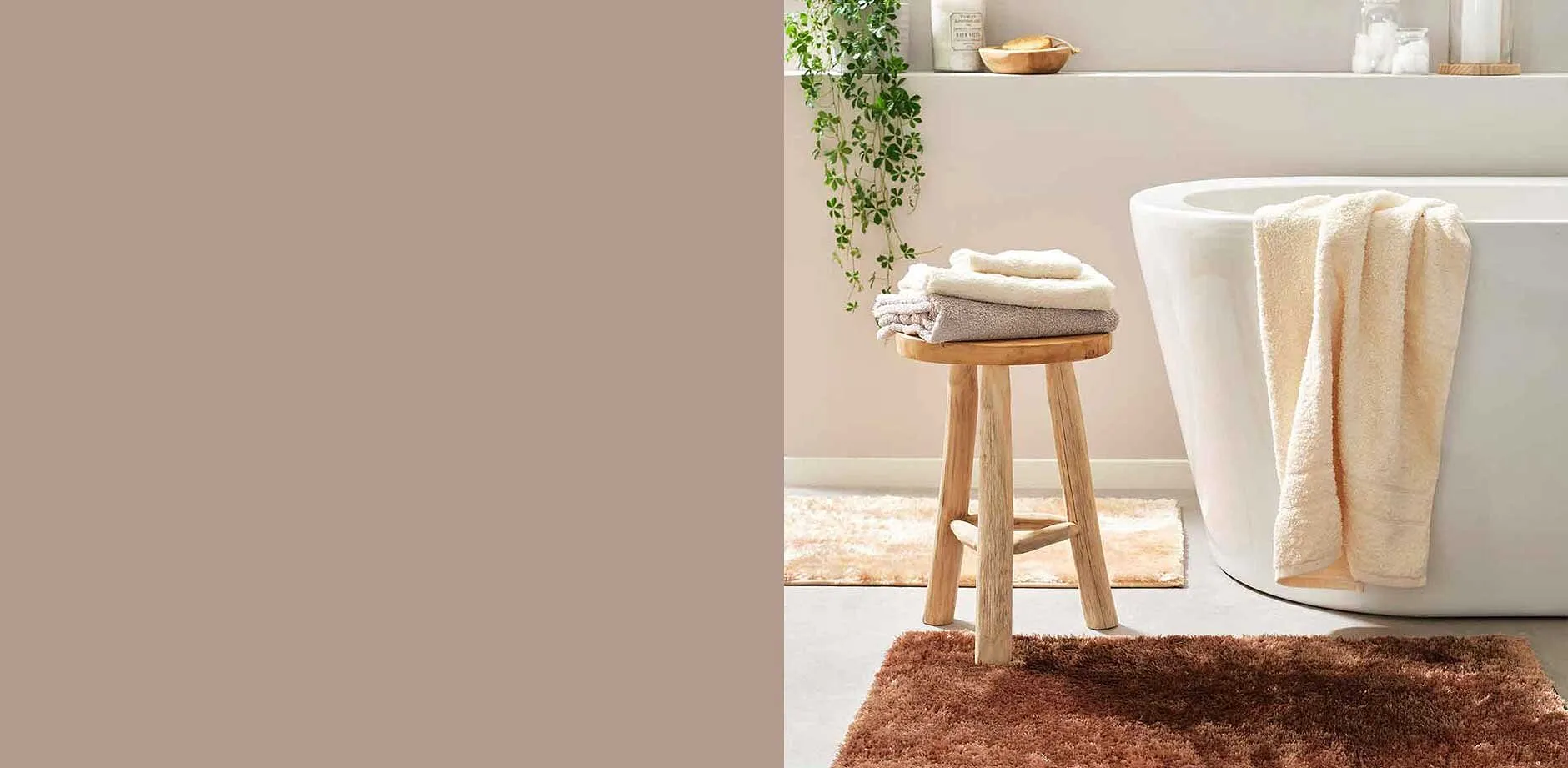 Badkuip met over de rand hangende, lichte handdoeken en krukje met handdoeken erop.