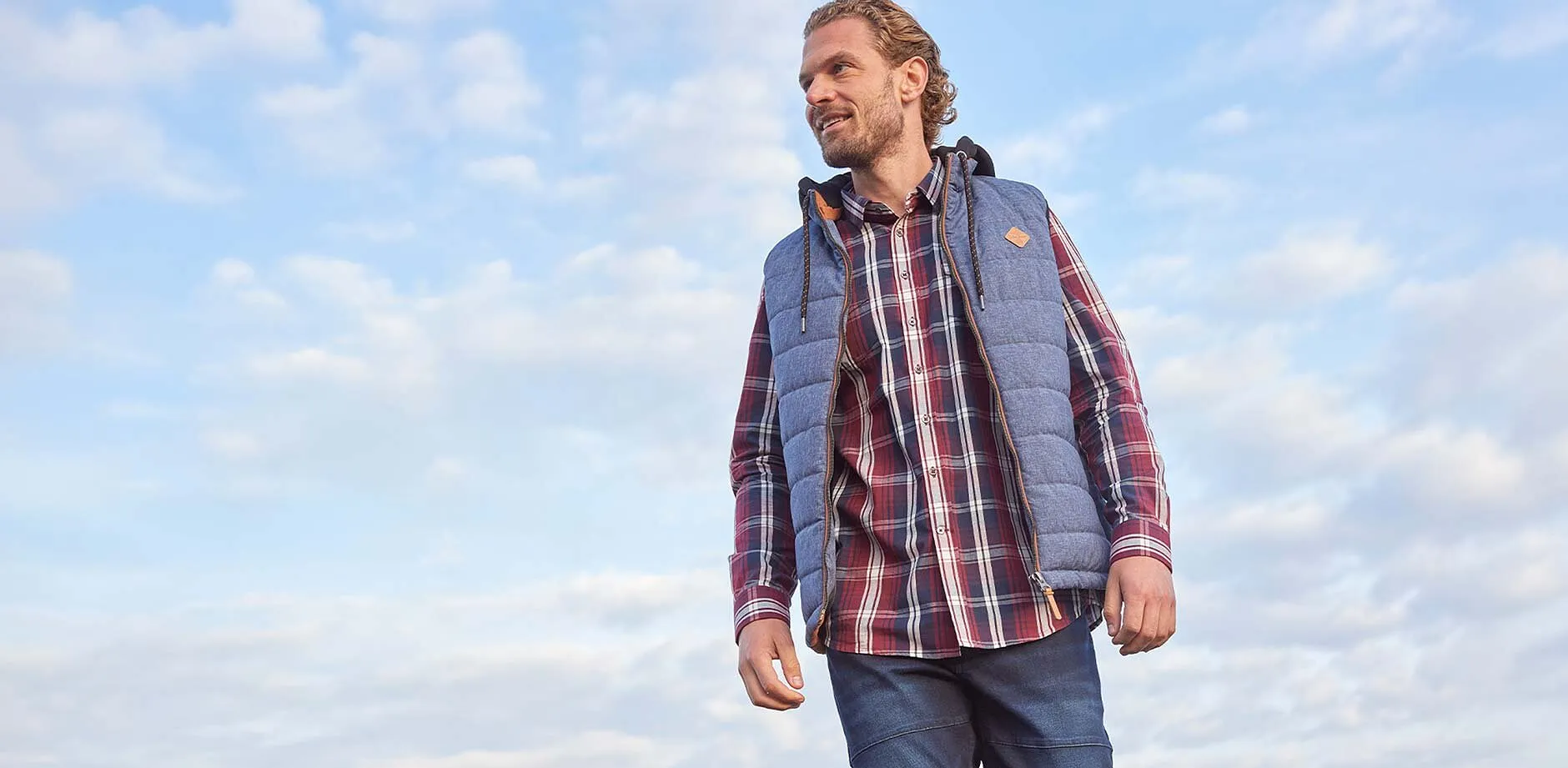 Geruit overhemd, blauwe jeans en grijze bodywarmer.