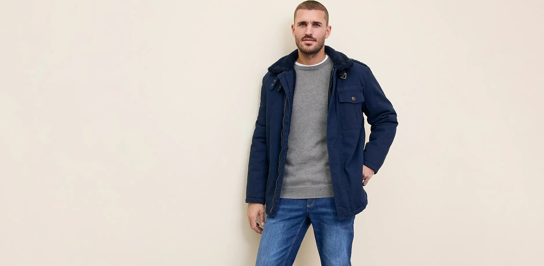 Donkerblauwe jas over grijze trui gecombineerd met blauwe jeans.