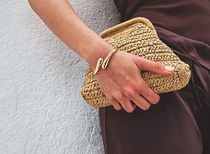 Elegantes braunes Kleid trifft auf sommerliche Strohclutch. Goldenes Armband als stilvoller Akzent.