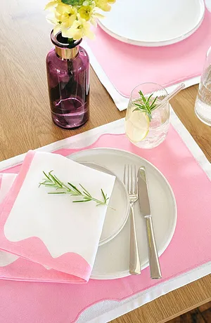 Zachtroze tafelkleed met een wit patroon siert de tafel. Verse bloemen en kruiden aanvullen de tafelsetting.