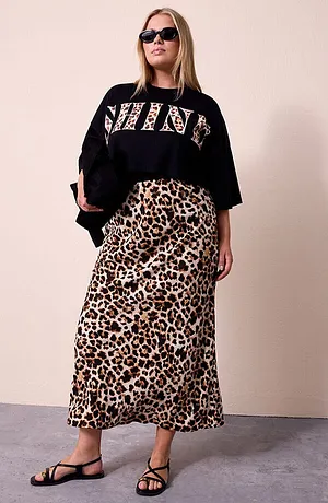 Frau mit schwarzem Cropped-Shirt mit SHINE-Leo-Schriftzug, passendem Rock im Leopardenmuster, schwarzer Sonnenbrille und schwarzer Glanz-Bag