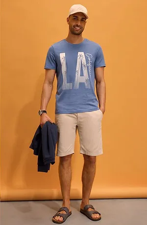 Blauw T-shirt met "LA"-print, lichte short, witte pet en sandalen. Een relaxte look voor de zomer.