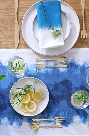 Een blauw tafellaken met een kleurverloop siert de tafel, aangevuld met wit servies en elegant bestek.