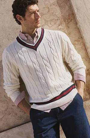 Witte trui met vlechtpatroon over een overhemd, gecombineerd met een jeans.