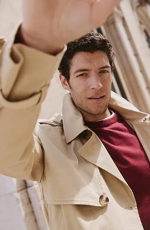 Elegante beige trenchcoat over een bordeauxrode trui.