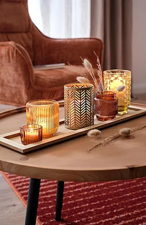 Een gezellige herfstsfeer met warme kaarsen en goudkleurige decoraties op een houten tafel.