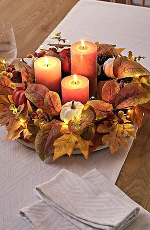 Tafeldecoratie in herfstkleuren bestaande uit kaarsen met daaromheen herfstbladeren op een witte tafelloper.