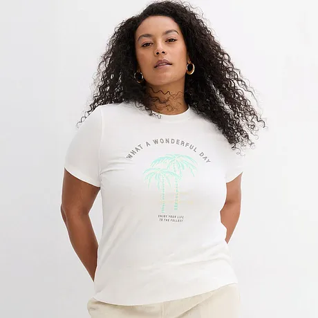 Wit T-shirt met groene palmenprint en tekst, casual gecombineerd met een lichte broek.