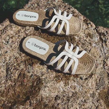 Zomerse sandalen met een gevlochten zool en witte bandjes liggen op een door de zon beschenen rots.