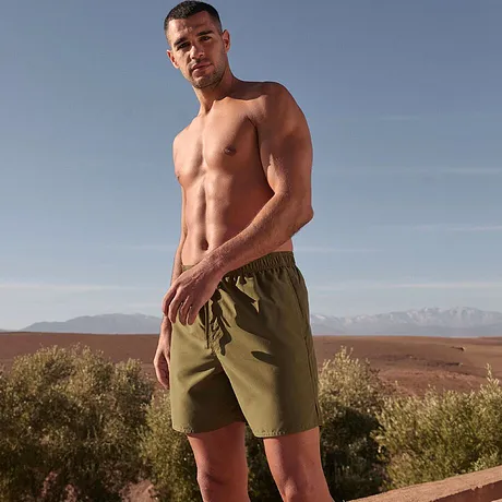 Olijfgroene badshorts benadrukken de atletische figuur.