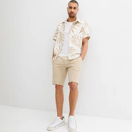 Zomerse outfit met beige shorts en een wit shirt met tropisch patroon.