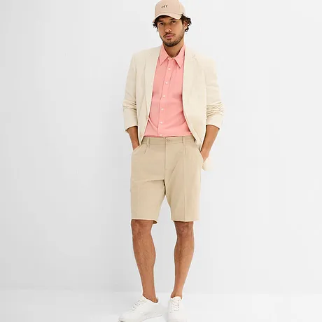 Elegante colbert in crème met een roze shirt, witte sneakers en een beige pet.