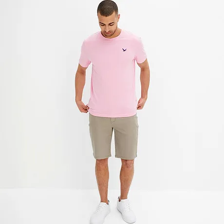 Een roze T-shirt met een klein logo en beige shorts vormen een zomerse outfit.