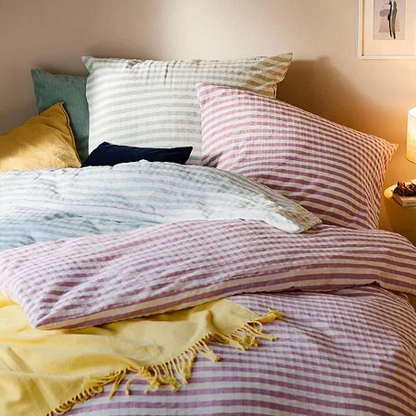 Gestreepte dekbedovertrekken in pastelkleuren sieren het comfortabele bed. Een gele deken zorgt voor kleuraccenten.