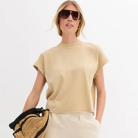 Sommerliches Outfit mit beigem Kurzarm-Oberteil, weißer Hose, Sonnenbrille und Strohtasche.