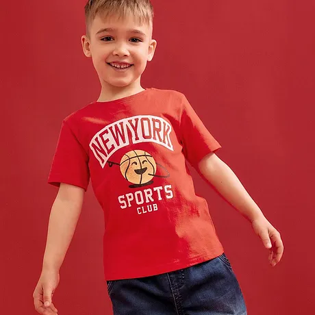 Rood T-shirt met "New York Sports Club" opdruk, gecombineerd met blauwe jeans.