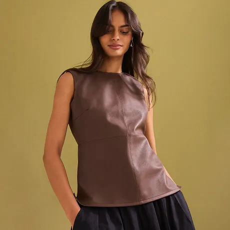 Elegante bruine imitatieleren top, gecombineerd met een donkere rok en subtiele oorbellen.