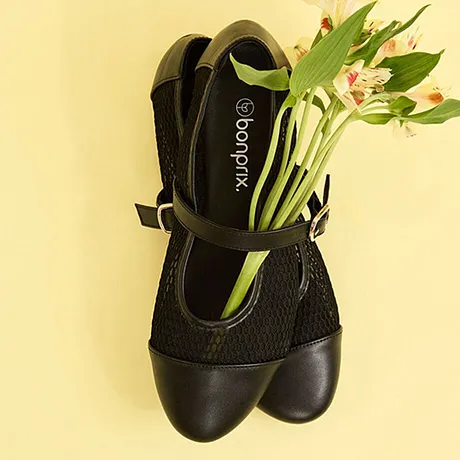 Zwarte dameschoenen met riemen en netstof, gevuld met verse bloemen.