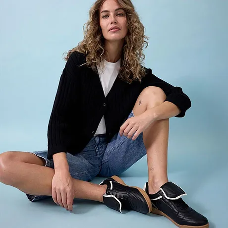 Zwarte jas, wit shirt, spijkershorts en stijlvolle zwarte sneakers.