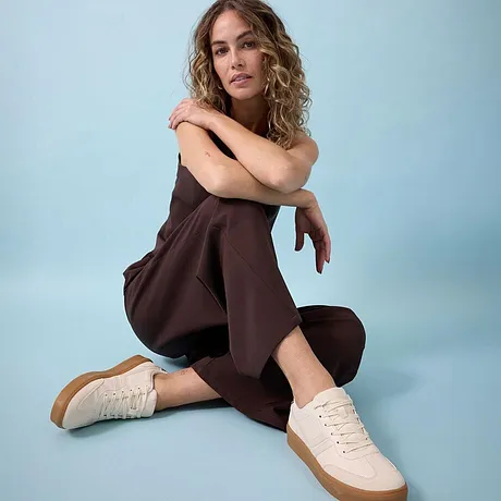 Bruine jumpsuit gecombineerd met crèmekleurige sneakers.