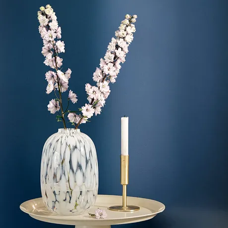 Elegante witte vaas met delicate kersenbloesems op een gouden dienblad, naast een slanke kaars.