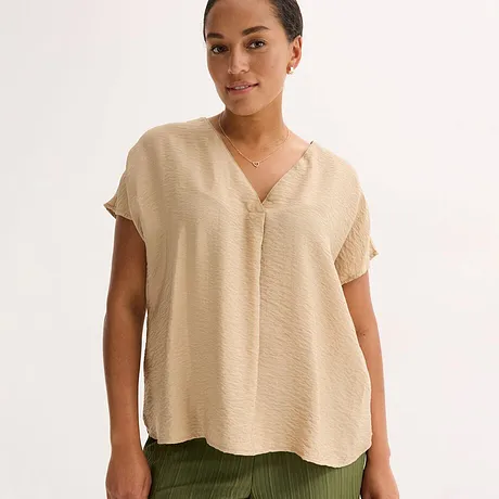 Beige, luchtige blouse met V-hals en korte mouwen, gecombineerd met een olijfgroene broek.