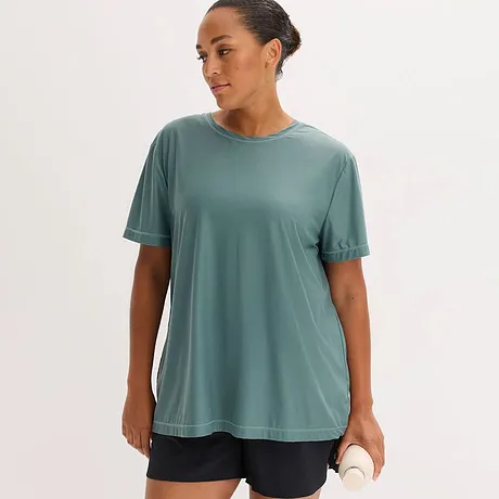 Een losvallend, saliegroen functioneel shirt met ronde hals en korte mouwen, gecombineerd met donkere shorts.
