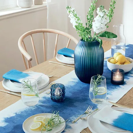 Een blauwe tafelloper siert de eettafel, contrasterend met witte borden en kleurrijke accessoires.