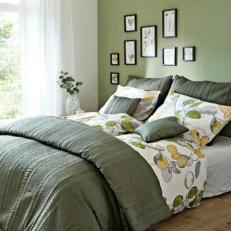 Gezellige slaapkamer met groen beddengoed en kussens. Bloemenpatroon op het beddengoed zorgt voor frisheid.