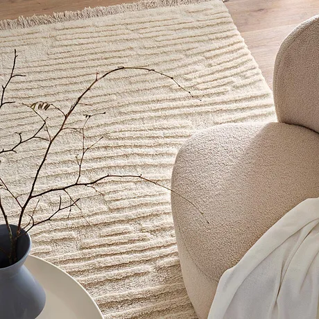 Gezellige woonkamer met een zachte vloerkleed, comfortabele fauteuil en een warme deken voor knusse momenten.