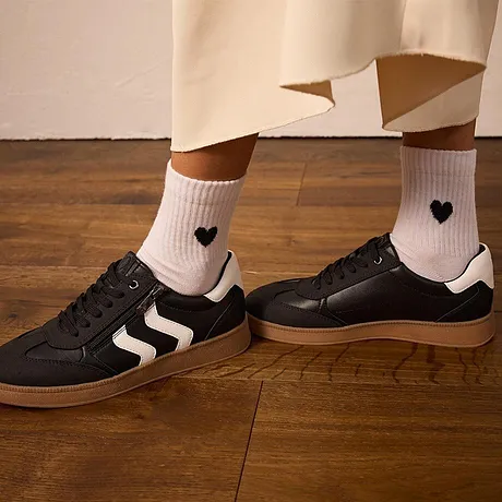 Witte sokken met hartjes, zwarte sneakers met witte strepen.
