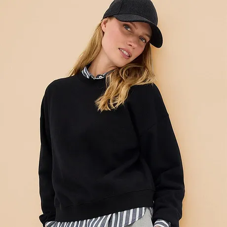 Zwart sweatshirt gecombineerd met gestreept overhemd en een casual baseballpet.