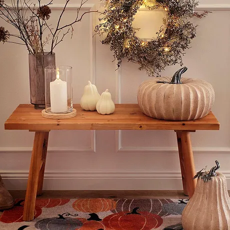 Decoraties voor de herfst op een houten bank: een brandende kaars, pompoenen en kaarsten zorgen voor een gezellige sfeer.
