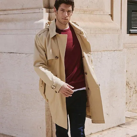 Elegante beige trenchcoat over een rode trui en een donkere jeans.