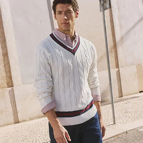 Witte gebreide trui met V-hals, donkere jeans en witte sneakers.