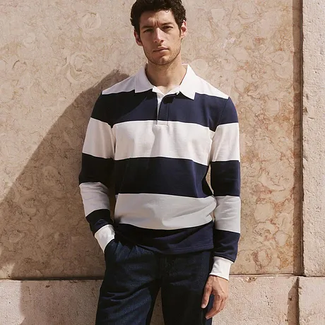 Klassieke look met een gestreepte rugby sweater, donkere broek en witte sneakers. 