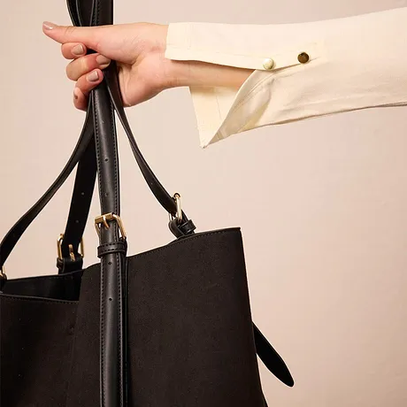 Hand houdt zwarte imitatieleren tas met lange hengsels vast.