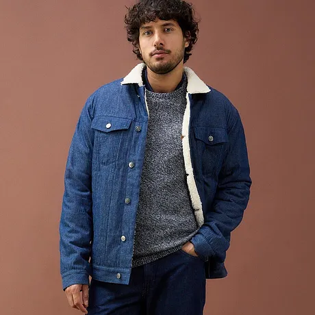Blauwe spijkerjas met fleece voering, grijze trui en donkere jeans.
