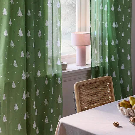 Feestelijk groen gordijn met witte dennenbomen zorgt voor een feestelijke kerstsfeer bij het raam.