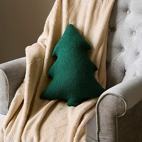 Fauteuil met crèmekleurige plaid en groen kussen in de vorm van een dennenboom.