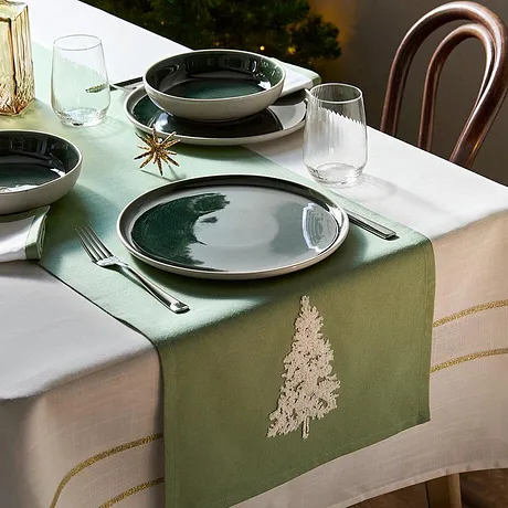 De tafelloper in groen met opgestikte dennenboom geeft je tafel tijdens de kerstdagen een extra feestelijk tintje.